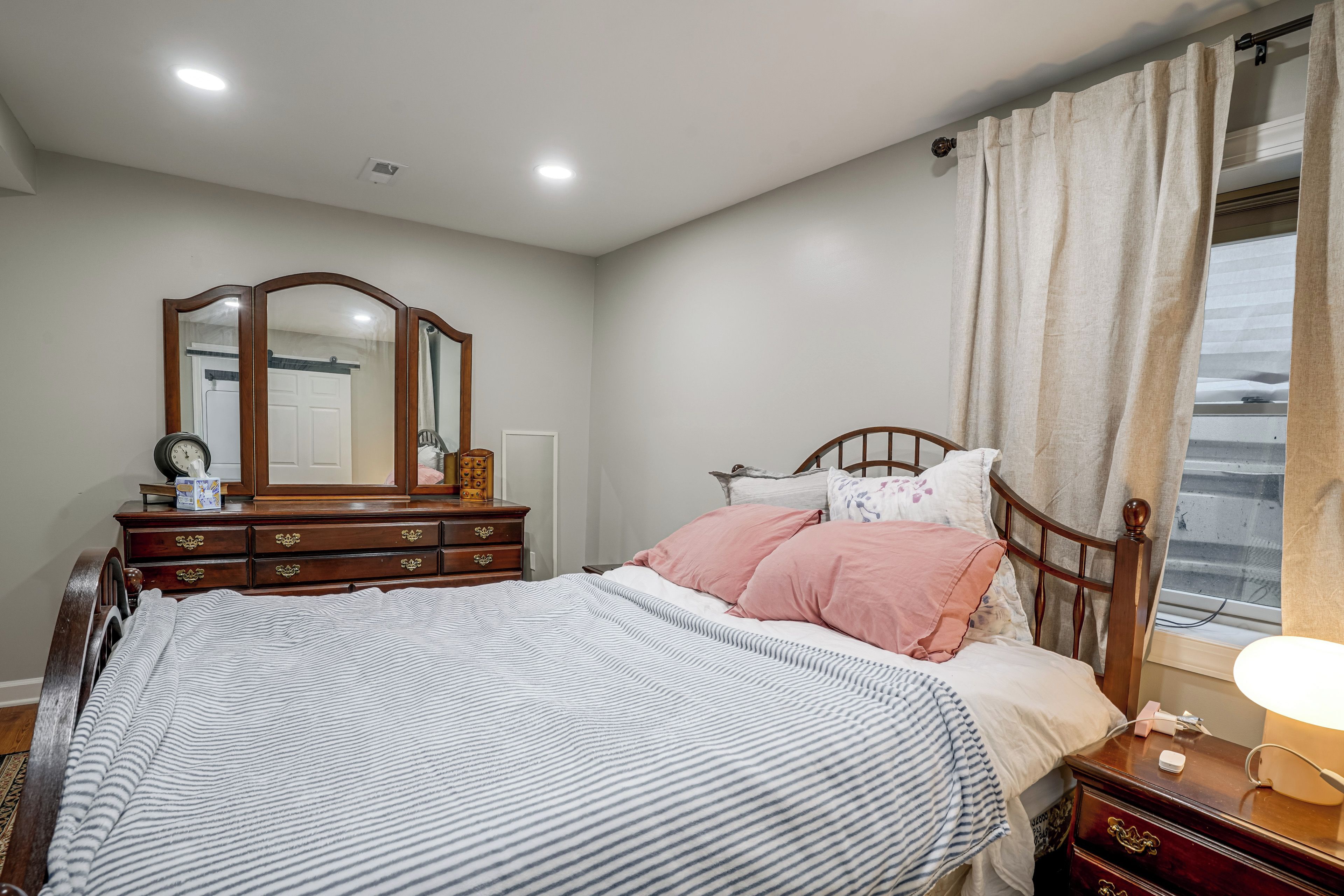Un dormitorio con cama, cómoda, espejo y ventana con cortinas.