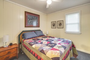 A bedroom with a bed, a nightstand, a lamp, a ceiling fan, and a window with blinds.