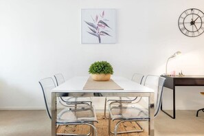 A modern dining area with a white table, clear chairs, a potted plant, a clock, and a desk with a lamp. - Cozy Studio CBD Stay Next to Darling Harbour (Sydney)