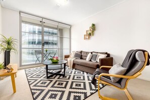 A modern living room with a sofa, armchair, and coffee table, large windows, and a geometric patterned rug. - Cozy Studio CBD Stay Next to Darling Harbour (Sydney)