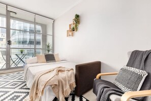 A modern bedroom with a large window, a bed with a beige blanket, a dark brown chair, and a small plant on the wall. - Cozy Studio CBD Stay Next to Darling Harbour (Sydney)