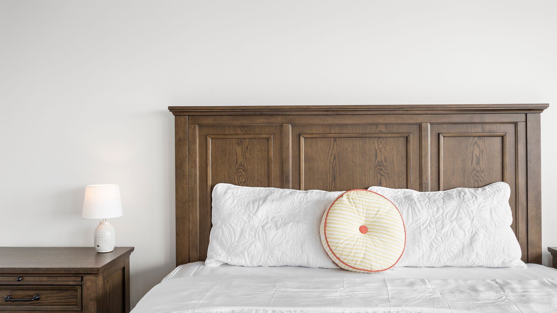 A bedroom with a wooden headboard, a white bedspread, and a bedside table with a lamp.