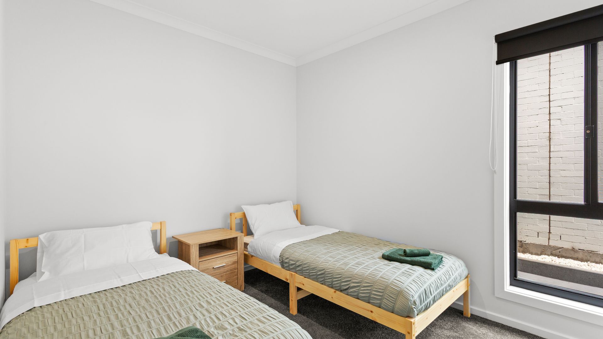 Ein Schlafzimmer mit zwei Einzelbetten, einem Holznachttisch und einem Fenster mit Blick auf eine Ziegelwand.