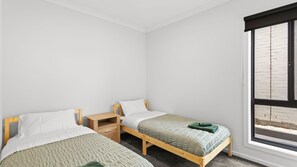 A bedroom with two single beds, a wooden nightstand, and a window with a view of a brick wall.
