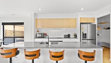 Une cuisine moderne avec un îlot central, des chaises en bois et un réfrigérateur en acier inoxydable.