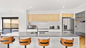 A modern kitchen with a central island, wooden chairs, and a stainless steel refrigerator.