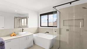 Un baño moderno con bañera, ducha y un espejo grande.