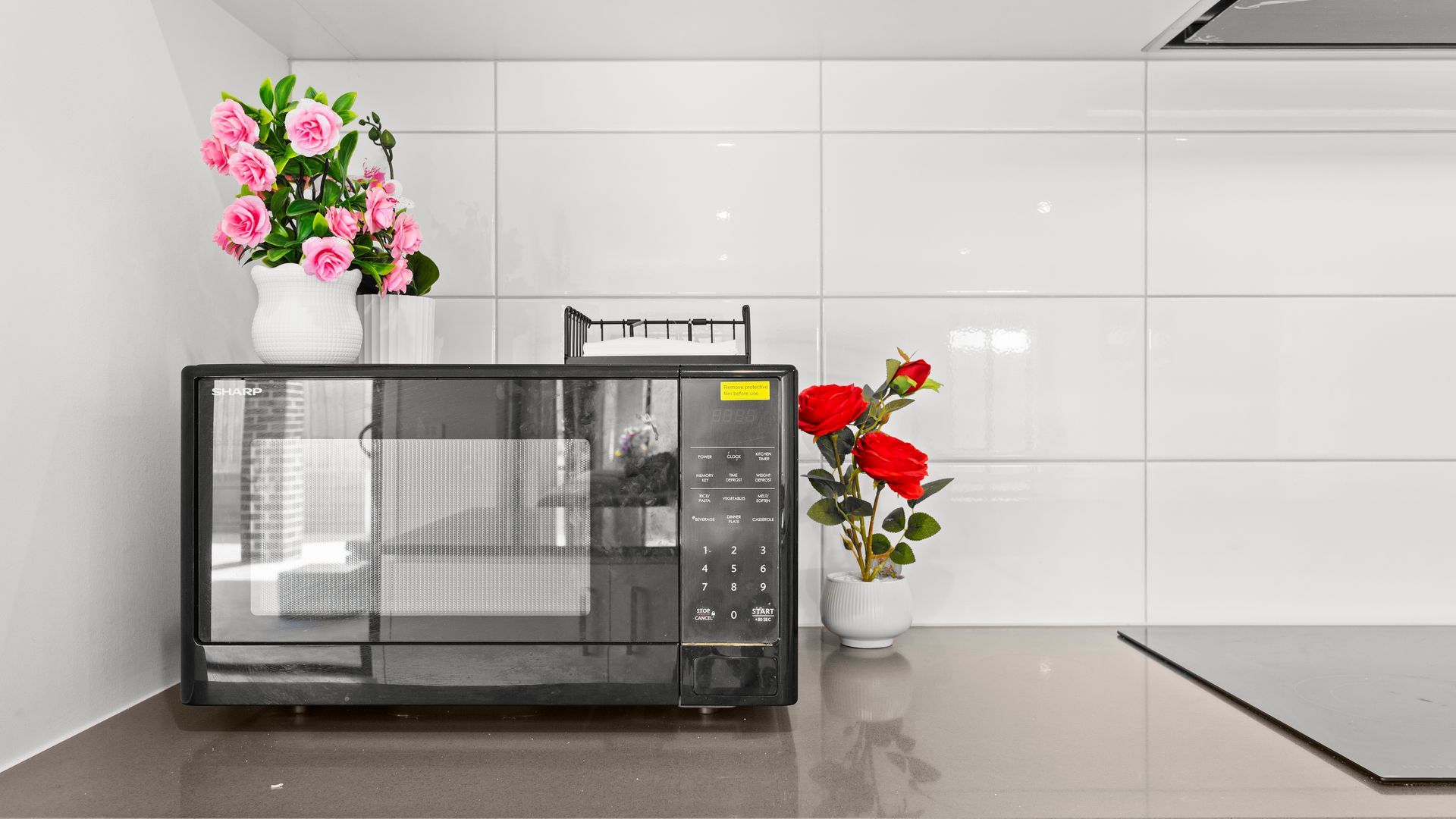 A microwave oven with a control panel, placed on a countertop in a kitchen with white tiles.