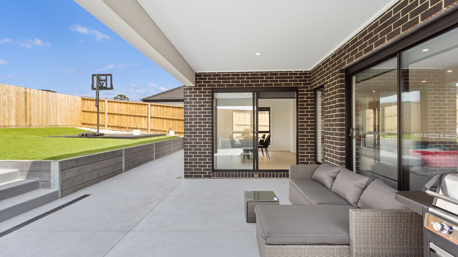 A covered patio area with a seating arrangement, a barbecue grill, and a view of the backyard.