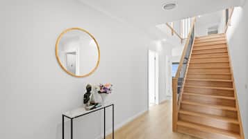 Ein modernes Interieur mit einer Holztreppe, einem runden Spiegel und einem kleinen Konsolentisch mit Buddha-Statue und Blumen.