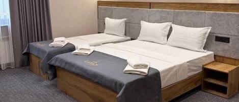 A hotel room with a double bed, a bedside table, a nightstand, and a window with curtains.