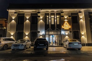 A hotel entrance with a prominent sign, a covered parking area, and a person at the door. - LAYAN HOTEL (Tashkent)