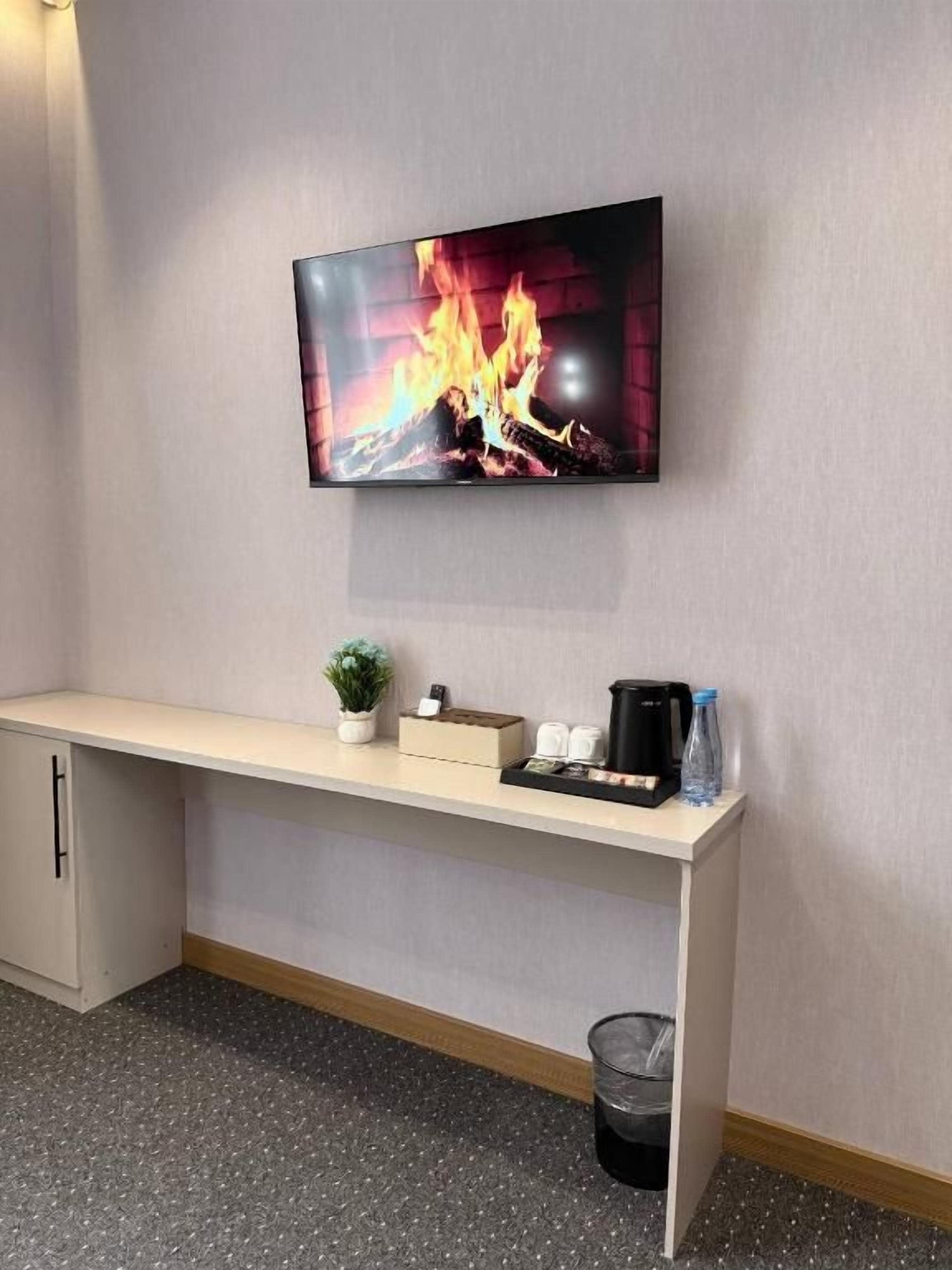 A flat-screen TV mounted on a wall above a wooden bench with a small plant, a coffee maker, and a water bottle.