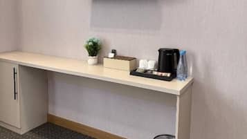 A flat-screen TV mounted on a wall above a wooden bench with a small plant, a coffee maker, and a water bottle.