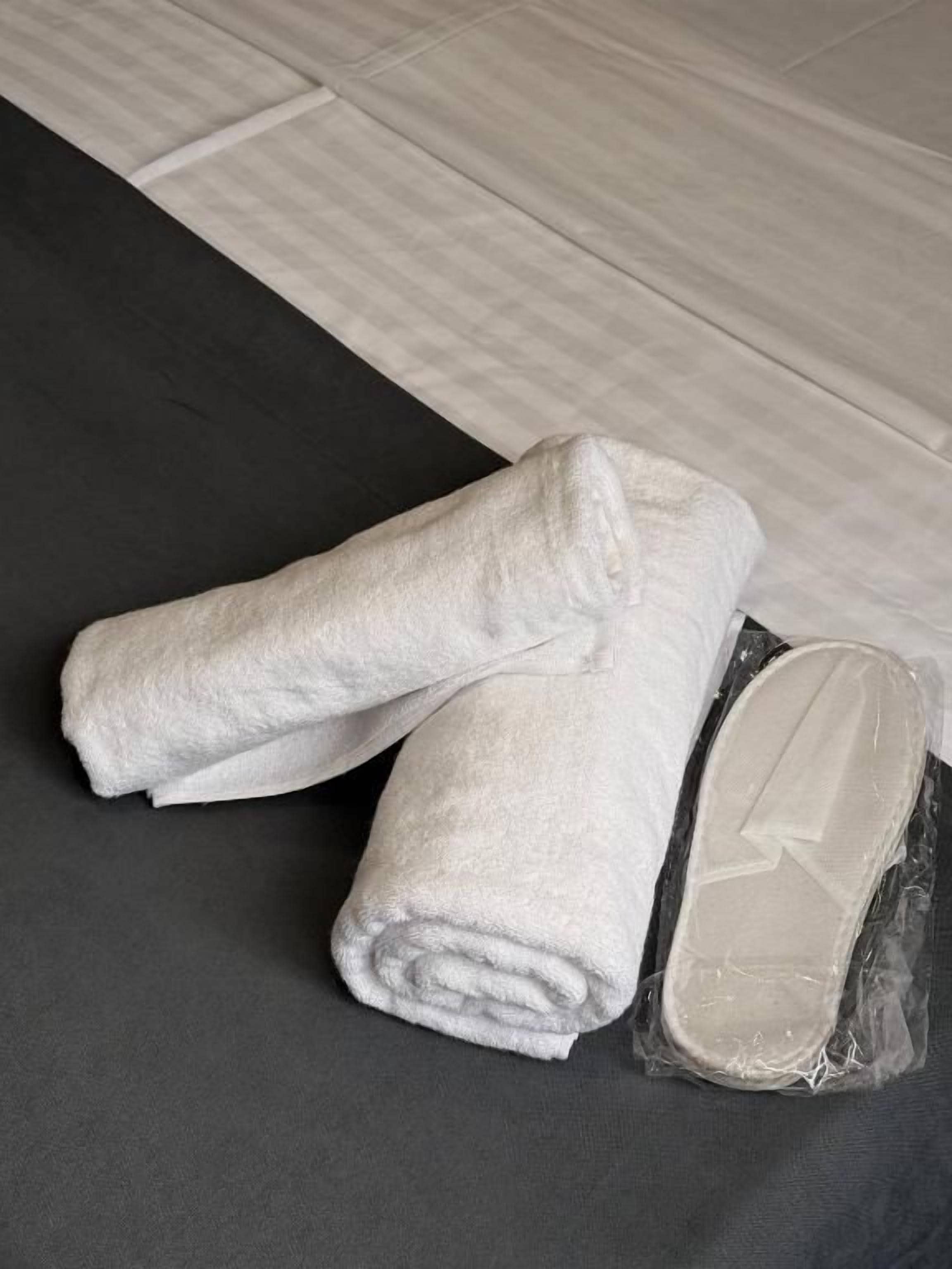 A neatly folded white towel and a plastic-wrapped item on a dark-colored surface.