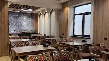 A restaurant with wooden tables and chairs, a patterned wall, and a large window.