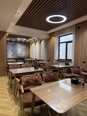 Een restaurant met houten tafels en stoelen, een patroonmuur en een groot raam.