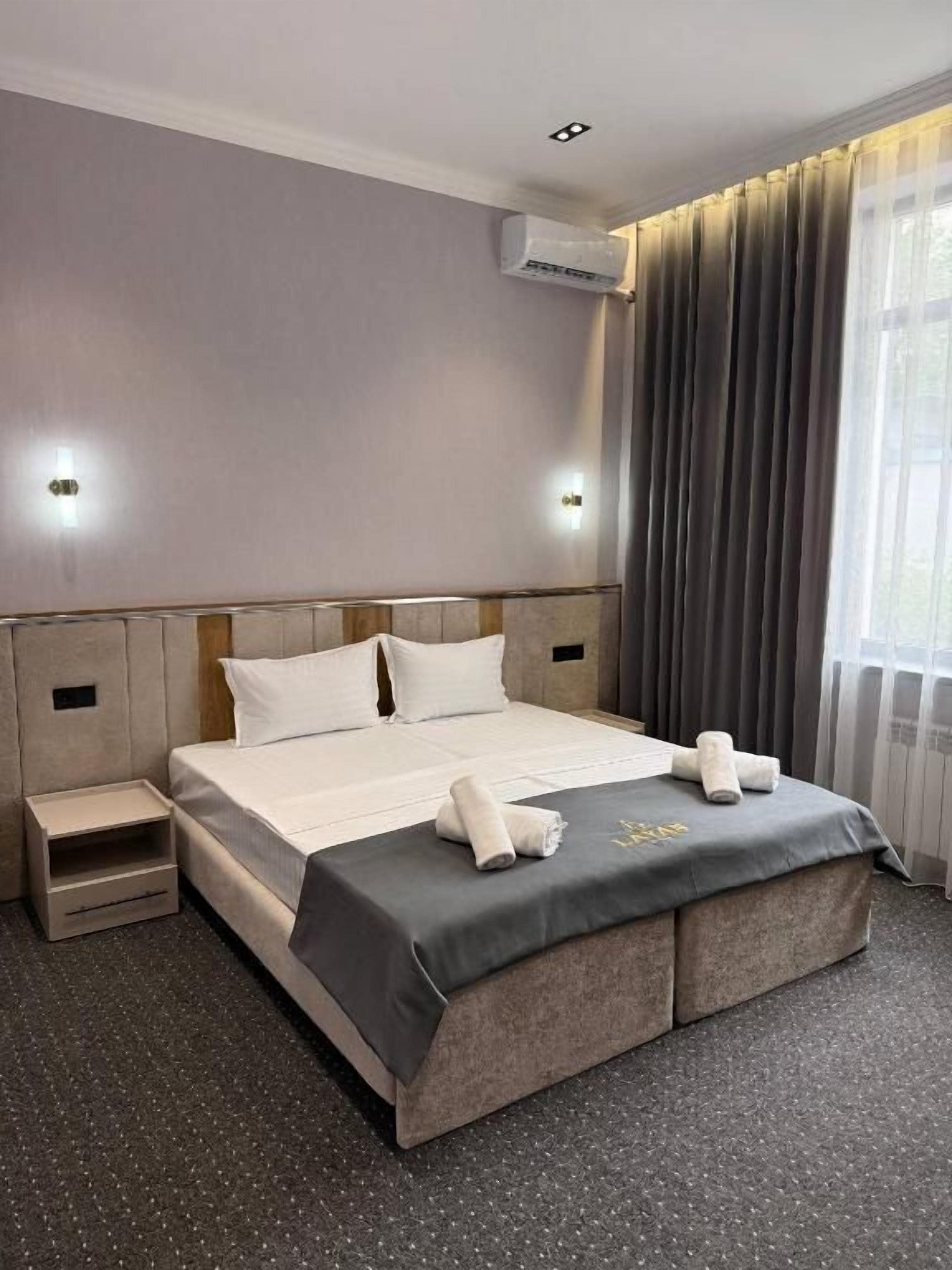 A hotel room with a bed, bedside tables, and a window with curtains.