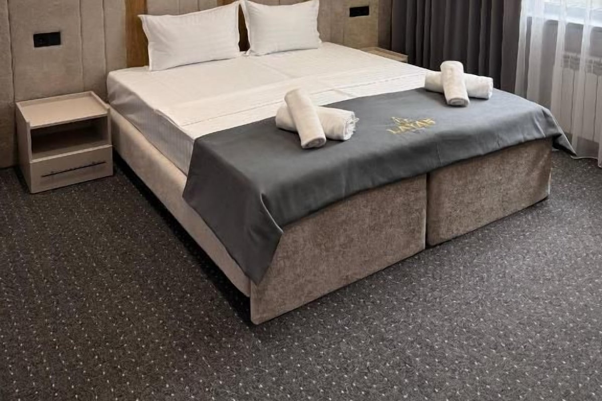 Habitació d'hotel amb un llit gran, taules de nit, una cadira incorporada i una finestra amb cortines.