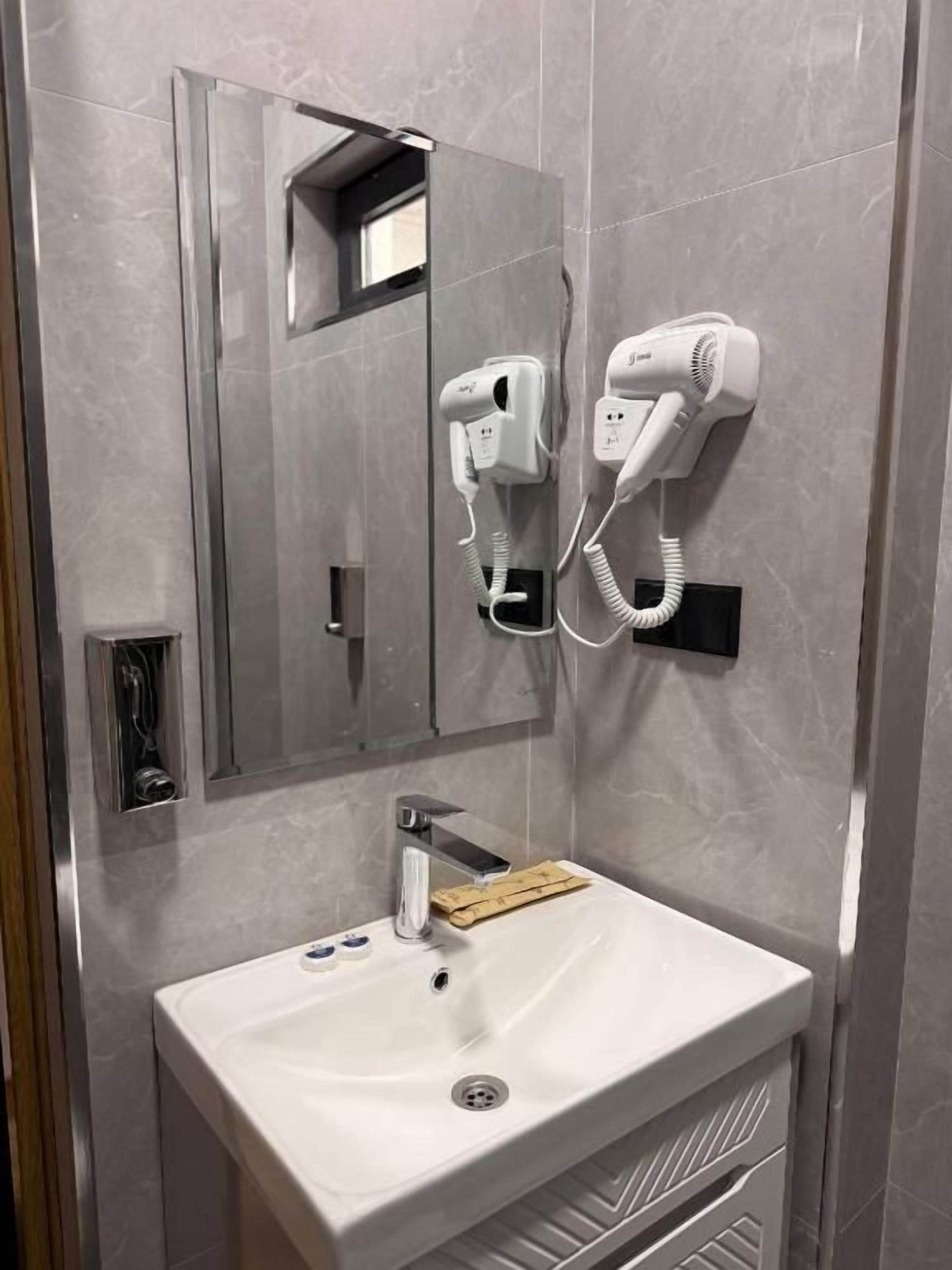 Un bany amb un lavabo blanc, un mirall i dos assecagats pel cabell penjats a la paret.