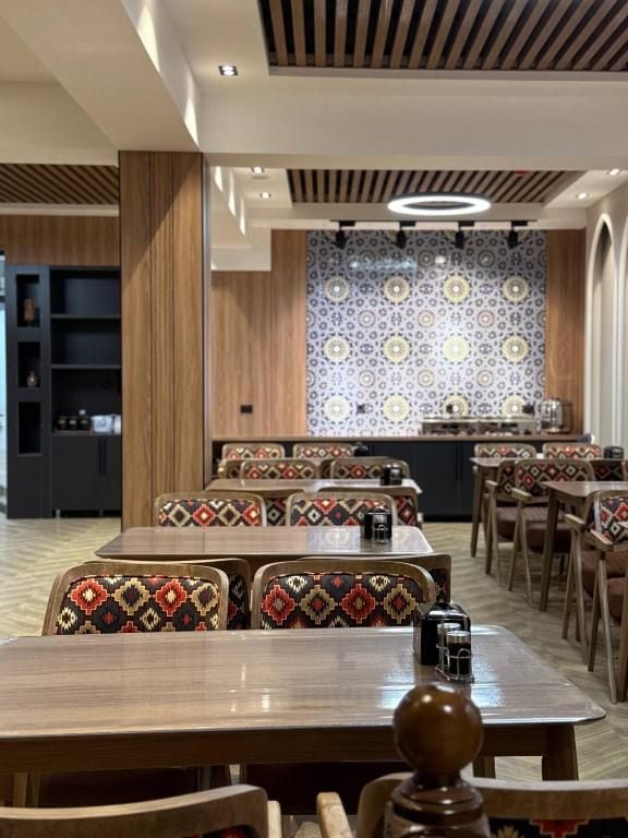 A dining area with wooden tables and chairs, patterned wall tiles, and a modern ceiling design.