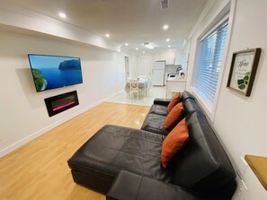 A modern living room with a black leather sofa, a flat-screen TV mounted on the wall, and a framed 'Home' sign on the wall. - Clean Spacious Vancouver home - Nanaimo skytrain - Trout Lake (Vancouver)