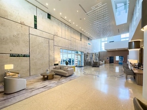 A spacious lobby with a high ceiling, modern furniture, and a large window providing natural light. - Resort-Style 2BR Beachfront Condo + Beach Access (Miami Beach)