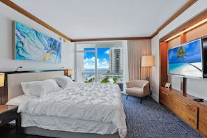Habitación de hotel con una cama grande, televisor, una silla y un balcón con vistas a edificios.