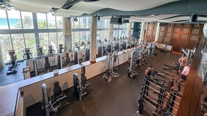 Et fitnesscenter med forskellig træningsudstyr, store vinduer og havudsigt.