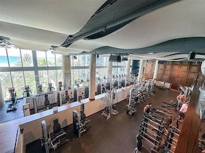 A gym with various exercise equipment, large windows, and a view of the ocean. - Resort-Style 2BR Beachfront Condo + Beach Access (Miami Beach)