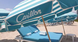 Ein Strand mit blau-weißen gestreiften Sonnenschirmen mit der Aufschrift 'Carillon' und Liegestühlen mit Handtüchern.