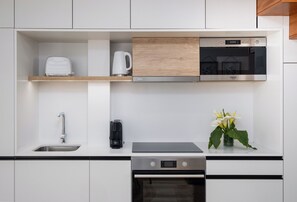 A modern kitchen with white cabinetry, a built-in oven, a microwave, a coffee maker, and a toaster. - Vidalii House (Ponta Delgada)