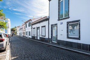 En kullerstensgata kantad av vita byggnader med svarta fönsterluckor och en blandning av olika arkitektoniska stilar.