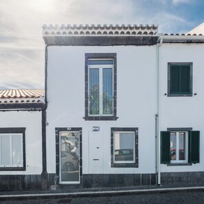 A building with a tiled roof, a central door, and two windows with shutters. - Vidalii House (Ponta Delgada)