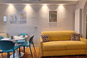 Una habitación con un sofá amarillo, una mesa de comedor con sillas y obras de arte en las paredes.