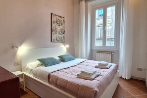A bedroom with a bed, a nightstand, a radiator, and a window with curtains. - Casa Mimosa is a typical old Florentine apartment, designed for the relaxation of our guests, we are in the lively central district Oltrarno.At Casa Mimosa you can find a kitchen living room with sofa bed and study corner, a bedroom with double bed, a ba (Florence)