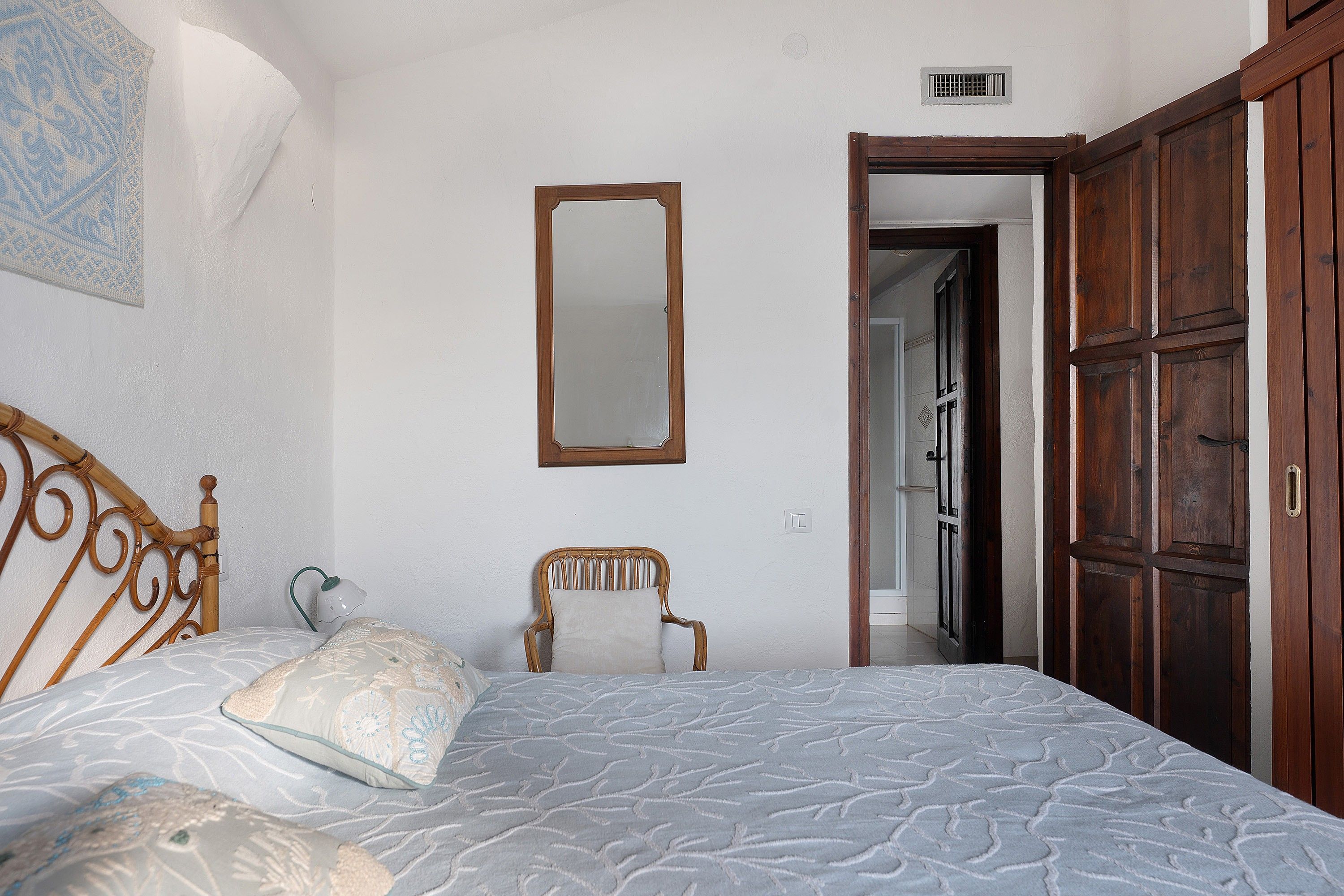 Ein Schlafzimmer mit einem Bett, einem Sessel, einem Holzschrank und einem Spiegel an der Wand.