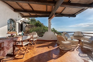 An outdoor terrace with hexagonal tiles, wicker furniture, and a view of the sea.