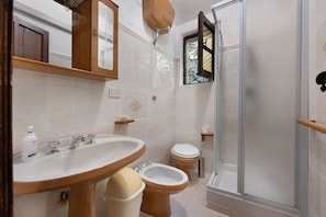 A bathroom with a sink, bidet, toilet, and a glass-enclosed shower.
