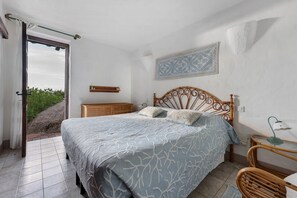 A bedroom with a bed, a nightstand, a chair, a window, and a wall-mounted shelf.