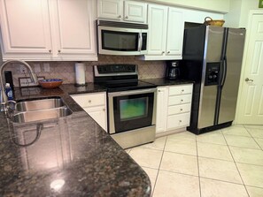 A kitchen with white cabinets, a stainless steel refrigerator, a microwave, an oven, and a sink. - Island Time - Gulf Front Retreat (2 Bed 2 Bath) (Pensacola)