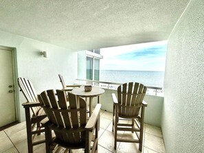 Ein Balkon mit zwei Adirondack-Stühlen, einem kleinen Tisch und Blick aufs Meer.