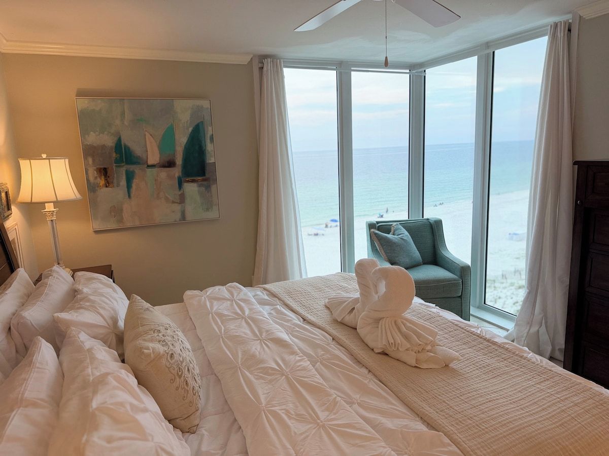 Ein Hotelzimmer mit Bett, Stuhl, einem Bild und Blick auf den Strand.