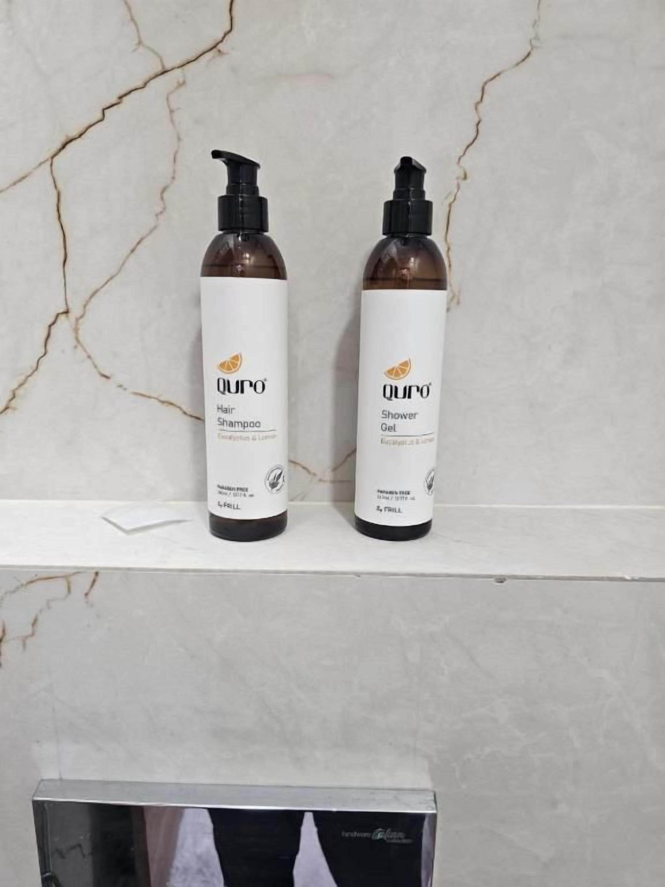 Dos botellas de cabello y gel de ducha Qu'ro sobre un estante de mármol.