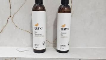 Dos botellas de cabello y gel de ducha Qu'ro sobre un estante de mármol.
