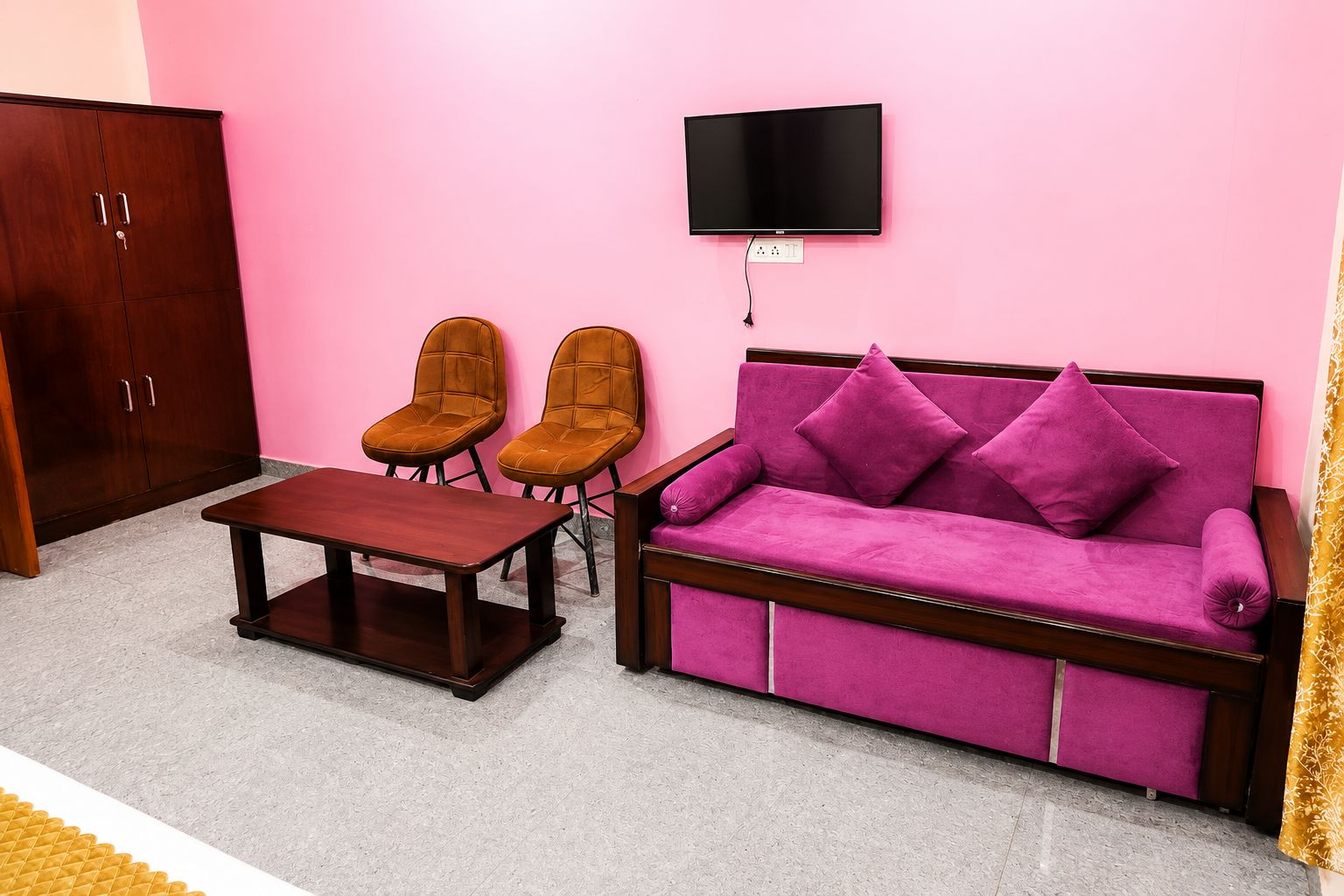 A living room with a sofa, two chairs, a coffee table, a TV mounted on the wall, and a wardrobe.
