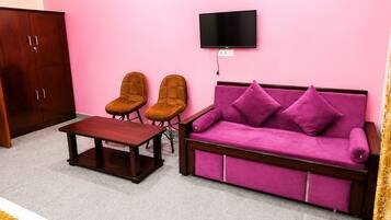 A living room with a sofa, two chairs, a coffee table, a TV mounted on the wall, and a wardrobe.