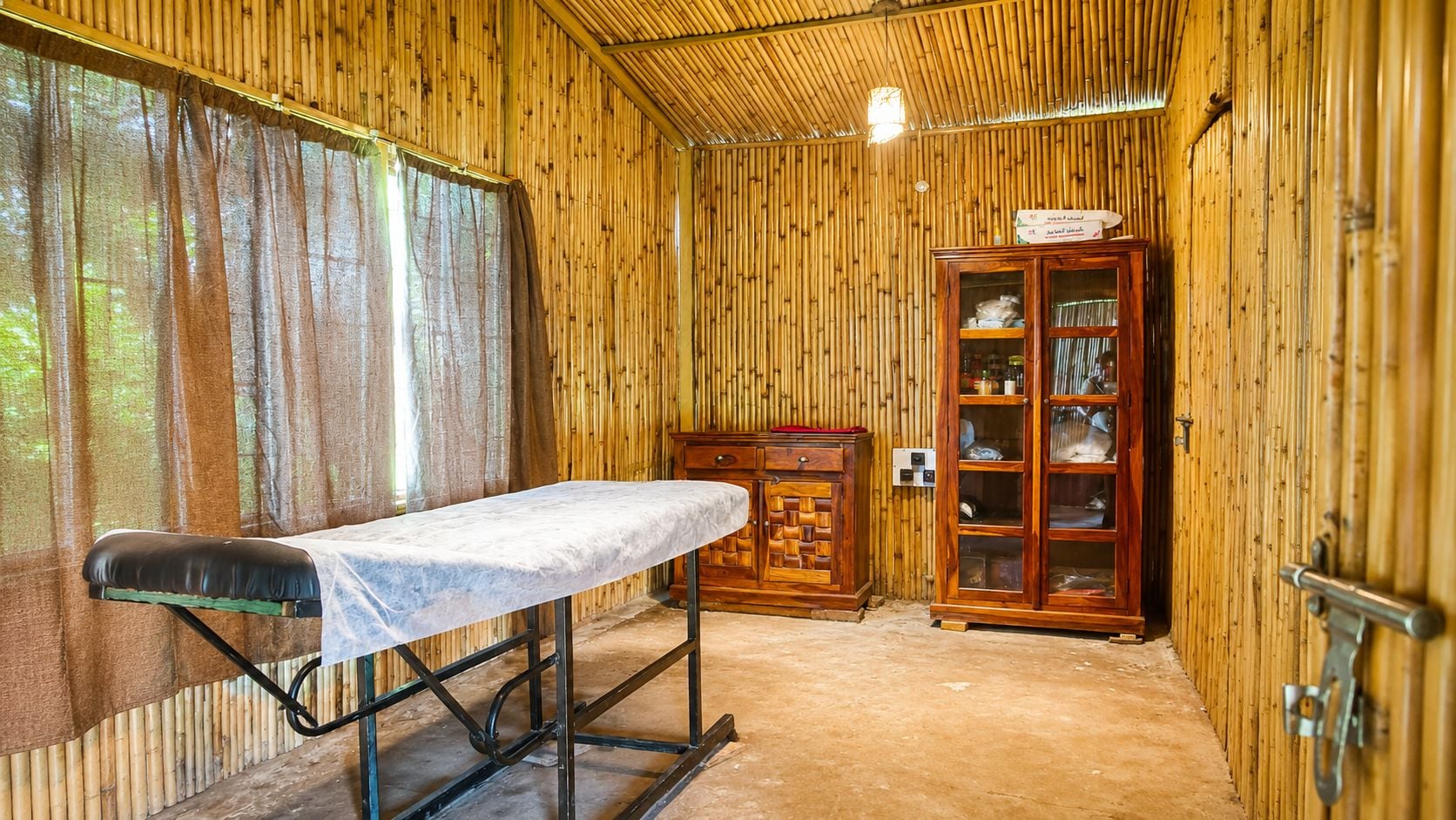 Una habitación con paredes de madera, una camilla de masaje, un armario y una ventana con cortinas.