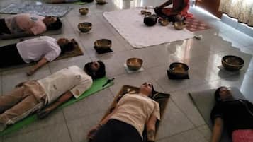 A group of people lying on mats in a room with a tiled floor, some bowls, and a wall with a framed picture.