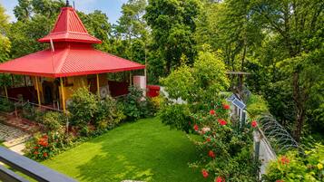 Ein pavillon mit rotem Dach, vor dem ein Garten liegt, umgeben von üppigem Grün und blauem Himmel.